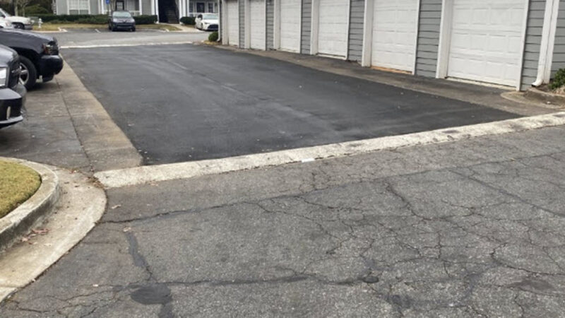 A building with six garage doors in a parking lot. In front of the building, the parking lot has had crack filling and pothole repair done.