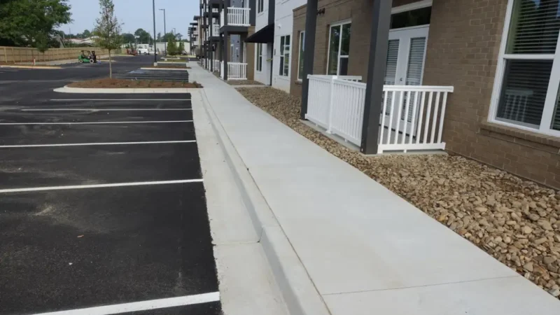 Photo of a parking lot that has been resealed and fresh striping applied, as well as a redone sidewalk with apartment buildings in the background.