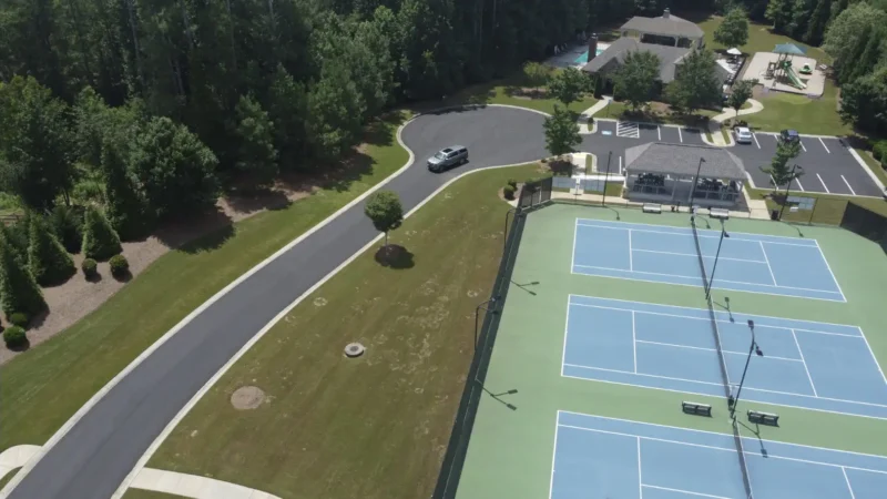 Aerial view of a neighborhood where the streets were milled and repaved. You can see the fresh, smooth blacktop in the photo, as well as 3 tennis courts and a park next to a clubhouse.