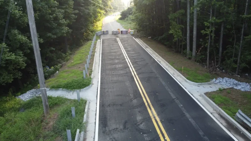 Photo of a road surrounded by trees with concrete stacks at the end.