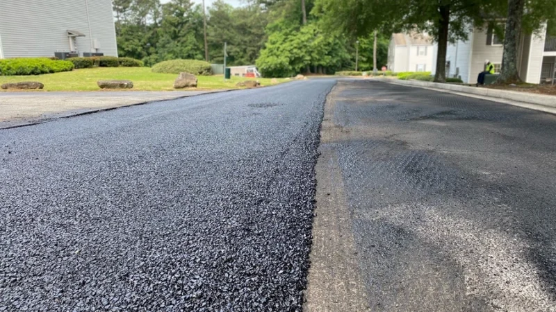 A road is seen with half of it repaved to show the difference in the old road and fresh road.